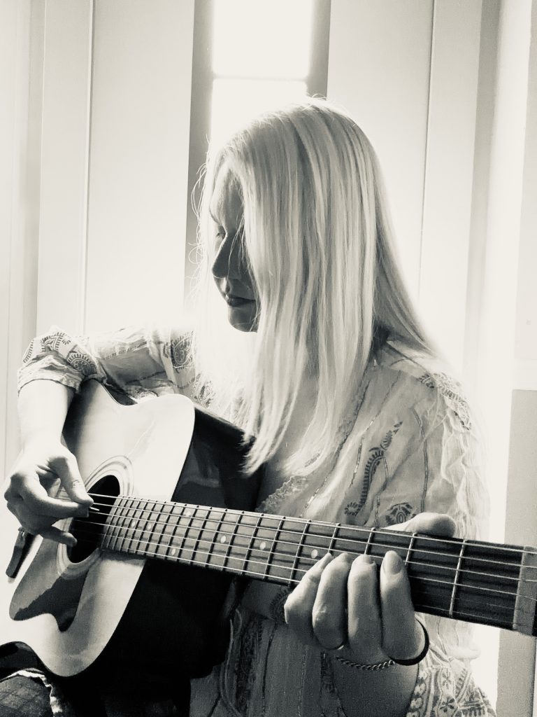 Kat Madleine mit ihrer Gitarre, Sie spielt If you knew what I knew, Das Licht ist seit von er linken Seite auf sie gerichtet. Sie schaut konzentriert nach links.